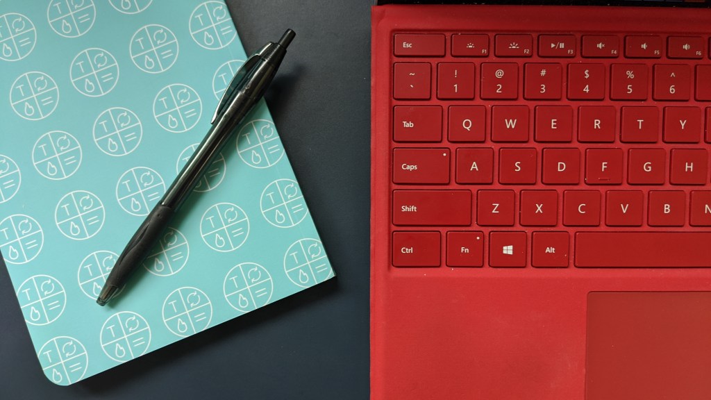 laptop keyboard next to a notebook and pen
