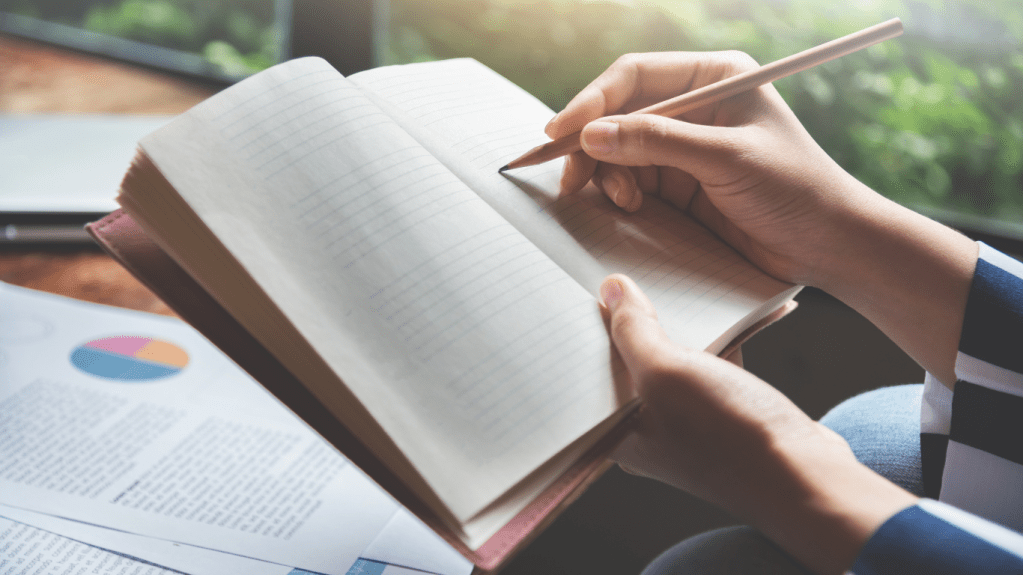 A woman taking notes in notebook while looking at data on a sheet of papers