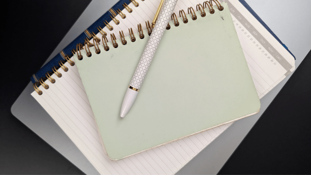 A white and gold pen on a stack of notebooks