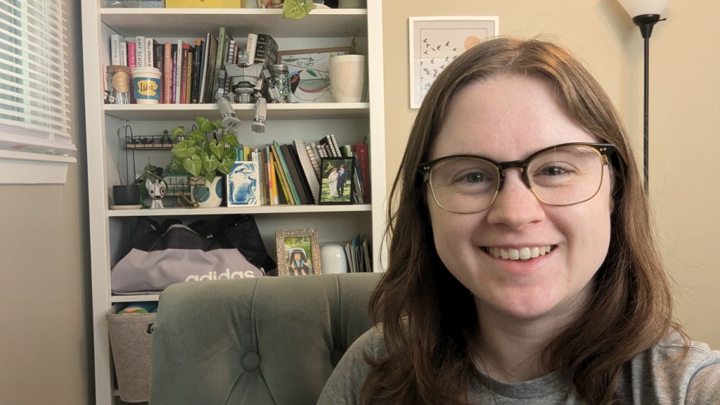 Alana smiling at the camera in her office with her bookshelf behind her